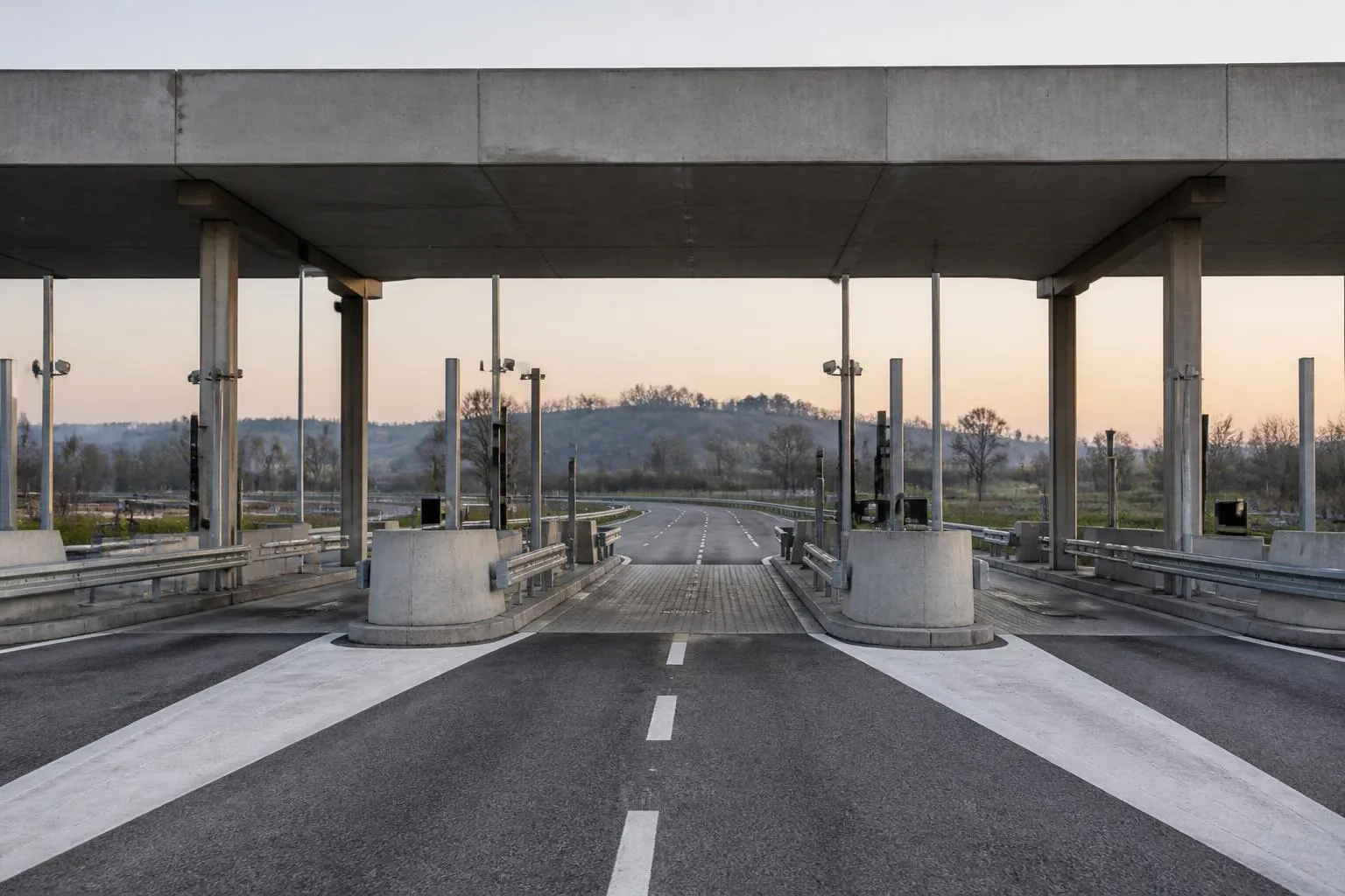 les voies d'un péage d'autoroute désert au petit matin, l'auvent de béton et les îlots de séparation