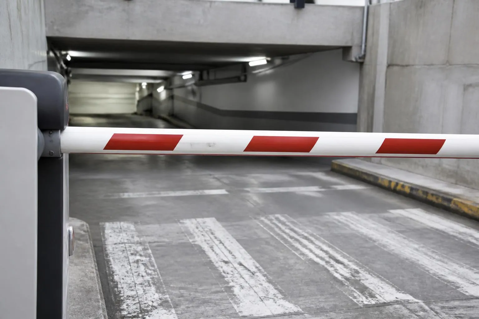 Barrière levante à l'entrée d'un parking souterrain en béton, rampe descendante éclairée au néon