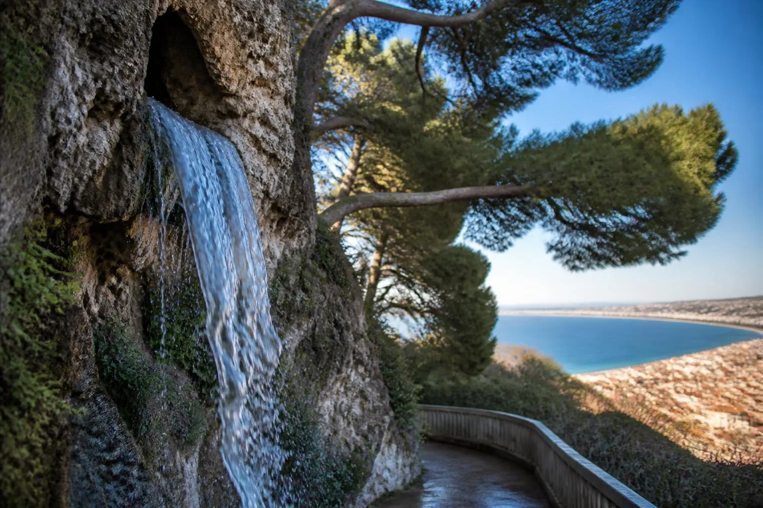 La cascade du Château à Nice tombant de sa grotte de rocaille entre les pins, la baie des Anges en contrebas