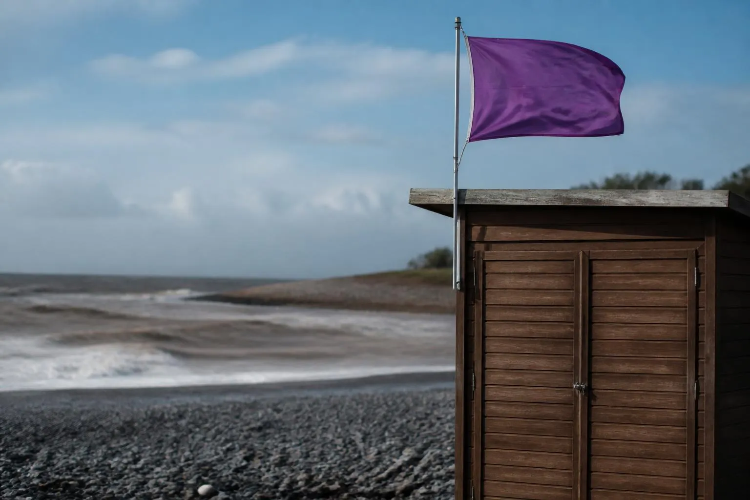Drapeau violet hissé au mât d'un poste de secours, plage de galets vide après la pluie