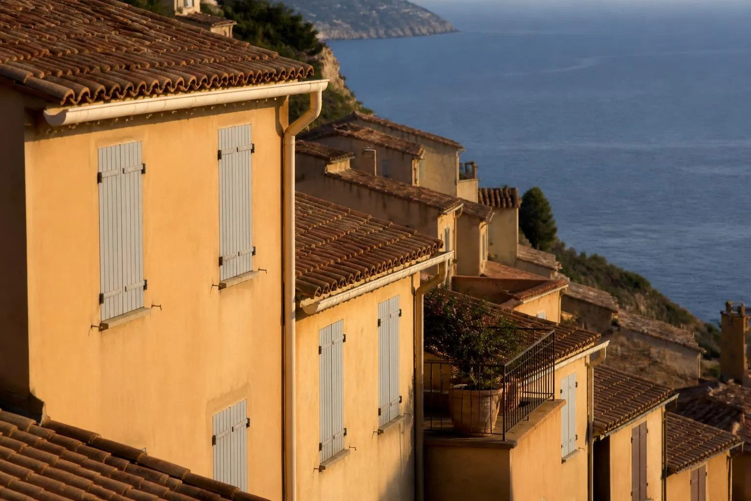 Immeubles en gradins sur une colline du littoral azuréen, volets clos et toits de tuiles, la mer au fond